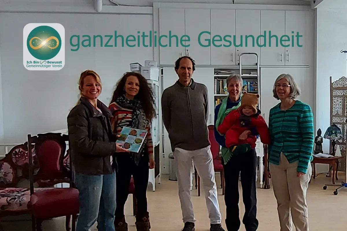 Fünf Erwachsene und ein Kleinkind stehen zusammen in einem hellen Raum, eine Frau hält eine Broschüre. Bildaufschrift: ganzheitliche Gesundheit.