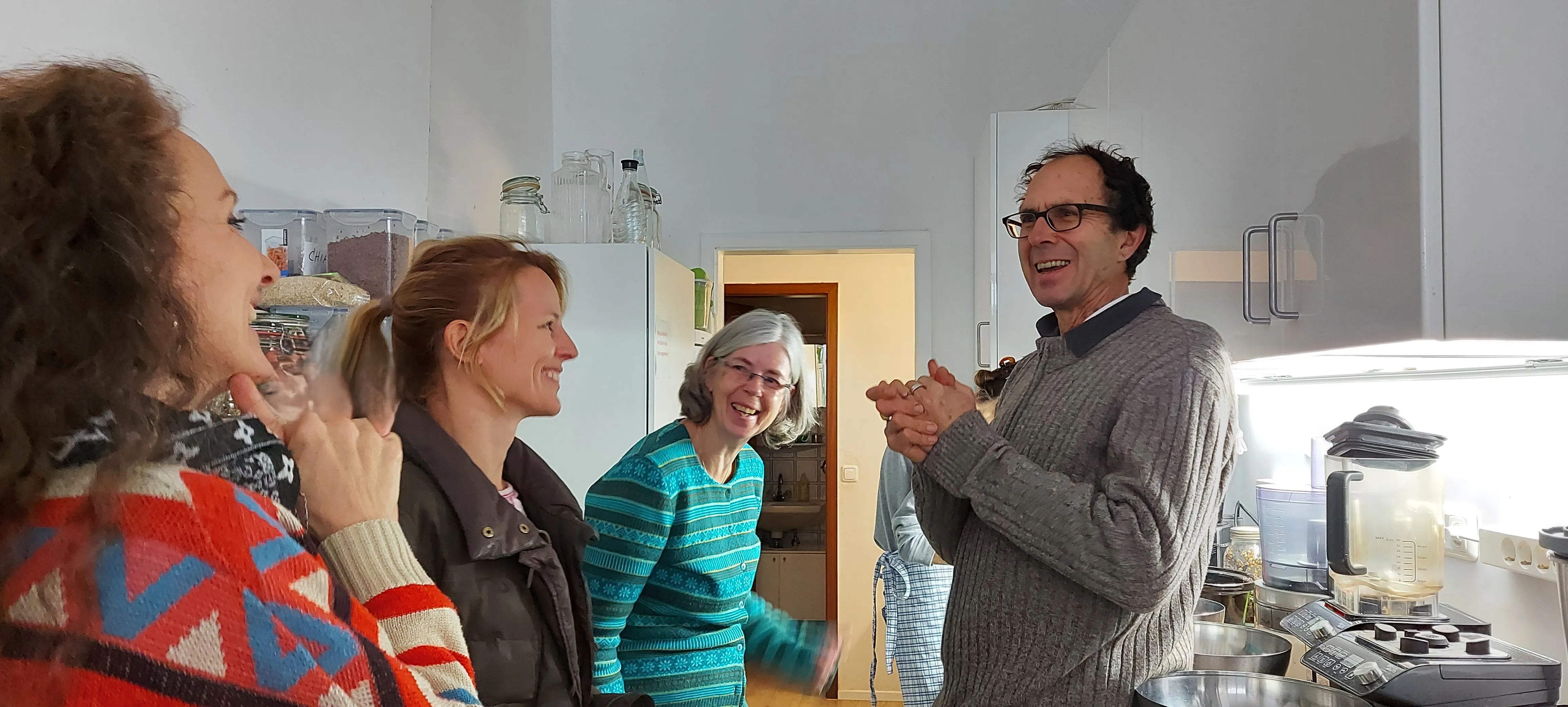 Dr. med. John Switzer und drei Frauen des Vereins stehen lachend in einer Küche mit Vitalkost-Zutaten zusammen.