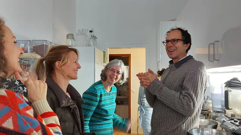 Dr. med. John Switzer und drei Frauen des Vereins stehen lachend in einer Küche mit Vitalkost-Zutaten zusammen.