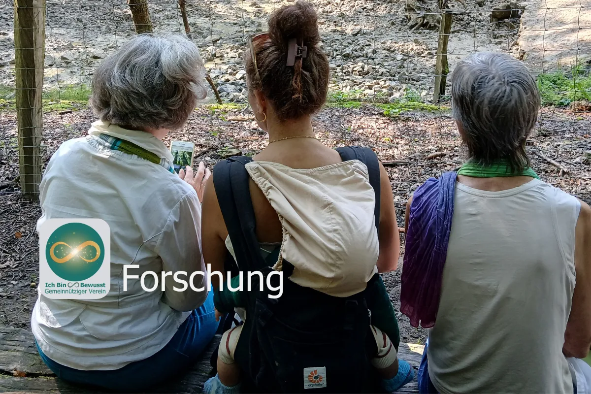 Drei Frauen sitzen von hinten auf einer Bank im Wald und schauen gemeinsam auf ein Handy. Bildaufschrift: Forschung.