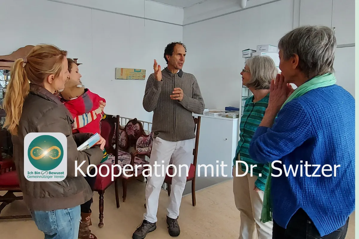 Dr. med. John Switzer im Gespräch mit einer Gruppe von Frauen in einem Raum. Bildaufschrift: Kooperation mit Dr. Switzer.